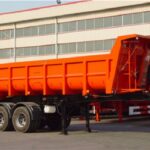 Orange dump semi-trailer parked outside a workshop