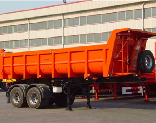 Orange dump semi-trailer parked outside a workshop