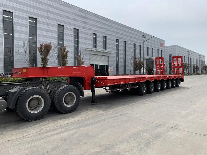 Red lowbed trailer with rear loading ramps outside a workshop